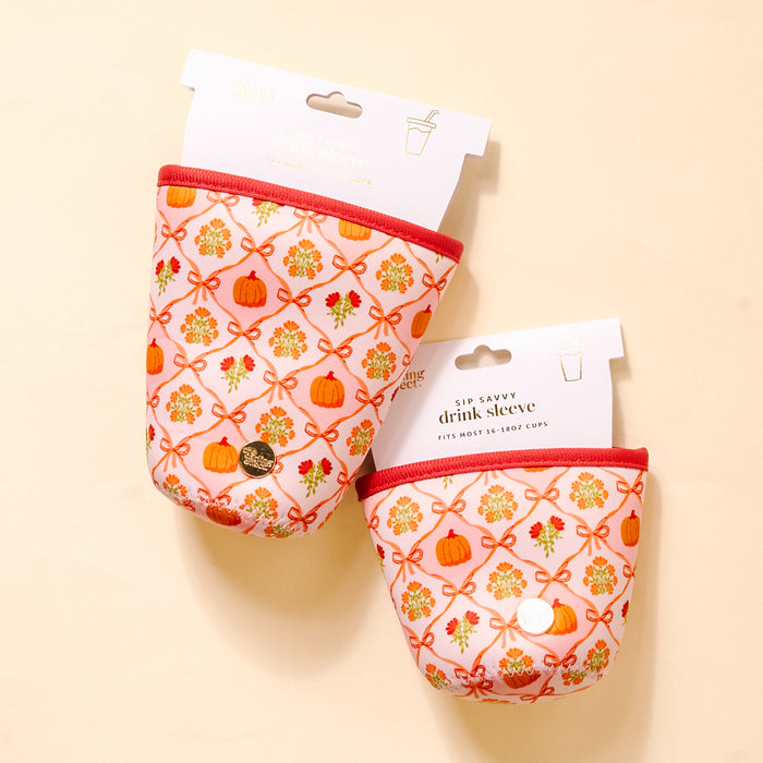 The Darling Effect's Patchwork Pumpkins Sip Savvy Drink Sleeve features a fall design with pumpkins, flowers, and red bows on light neoprene. Each sleeve comes packaged and displayed on beige—perfect for seasonal drinks.