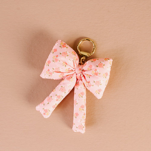 The Darling Effect's Peachy Petals Puffy Bow Bag Charm is a coquette-inspired keychain with an oversized pink floral bow and gold clasp, perfect for accessorizing your bag. Shown on a light beige background.