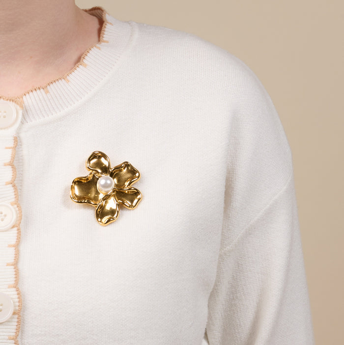 A person wears a white cardigan with scalloped edges and large buttons, styled with The Darling Effect's Pearl Core Flower Timeless Brooch pinned on the chest.