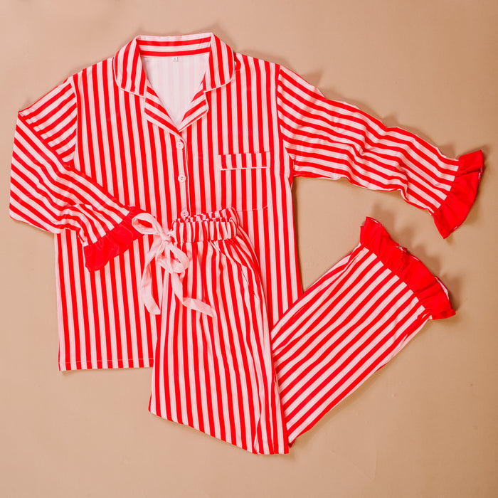 The Darling Effect’s Peppermint Stripes Sweet Dreams Pajama Pants Set features red and white stripes, a button-up collared top with ruffle trim, and drawstring pants—perfectly cozy for relaxing nights. Laid flat on a beige background.