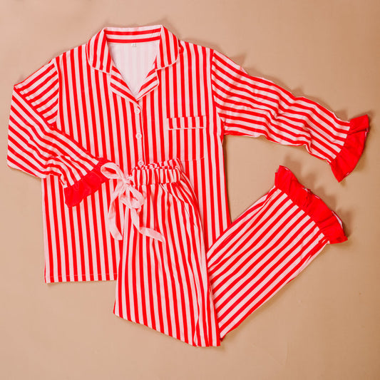 The Darling Effect’s Peppermint Stripes Sweet Dreams Pajama Pants Set features red and white stripes, a button-up collared top with ruffle trim, and drawstring pants—perfectly cozy for relaxing nights. Laid flat on a beige background.