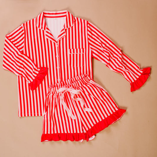 The Darling Effect’s Peppermint Stripes Sweet Dreams Pajama Shorts Set features red and white stripes, a long-sleeve button-up top, matching ruffled-trim shorts with a white ribbon tie, all made from ultra-soft fabric.