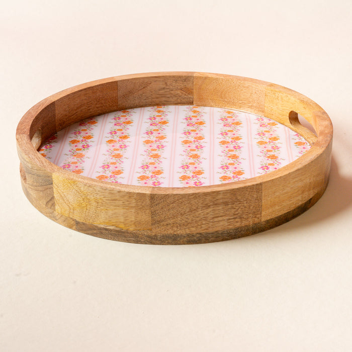 The-darling-effect’s Petal Parade Pink Large Round Wood Enamel Tray features two handle cutouts and a floral pink-and-orange pattern on white, shown here atop a light-colored surface.