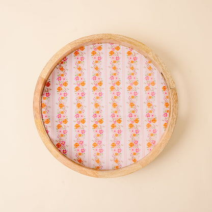 The Petal Parade Pink Large Round Wood Enamel Tray by the-darling-effect features vertical rows of orange and pink florals on a pink base, adding vibrant charm to any setting. Shown on a light beige background.