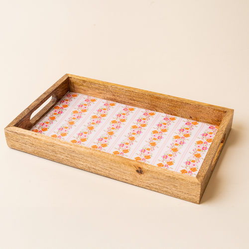 The-darling-effect’s Petal Parade Pink Rectangle Wood Enamel Tray features cut-out handles and a white interior with orange and pink floral stripes on a cream background.