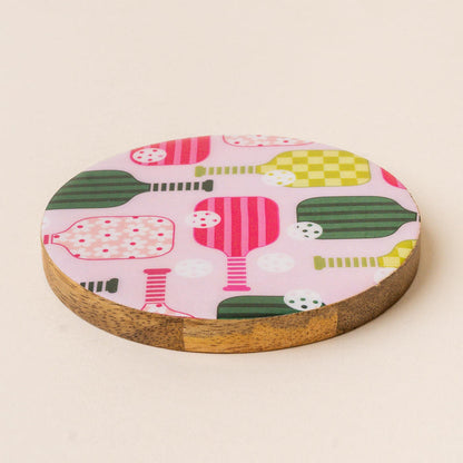The-darling-effect’s Pickleball Party Wood Enamel Coaster features a pink surface with vibrant pickleball paddle and ball designs, adding playful style and everyday durability to your decor.