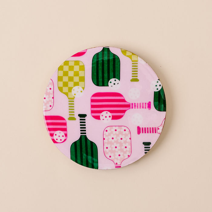 The Pickleball Party Wood Enamel Coaster by the-darling-effect features colorful pink, green, and white paddle and ball designs on light pink—an eye-catching way to add charm to your table.