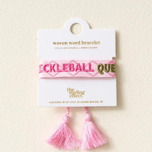 The Darling Effect's Pickleball Queen Woven Bracelet features pink embroidery and tassels, is fully adjustable, and comes on a white card. Designed in Grand Rapids, MI—perfect for fans of trendy embroidered bracelets.