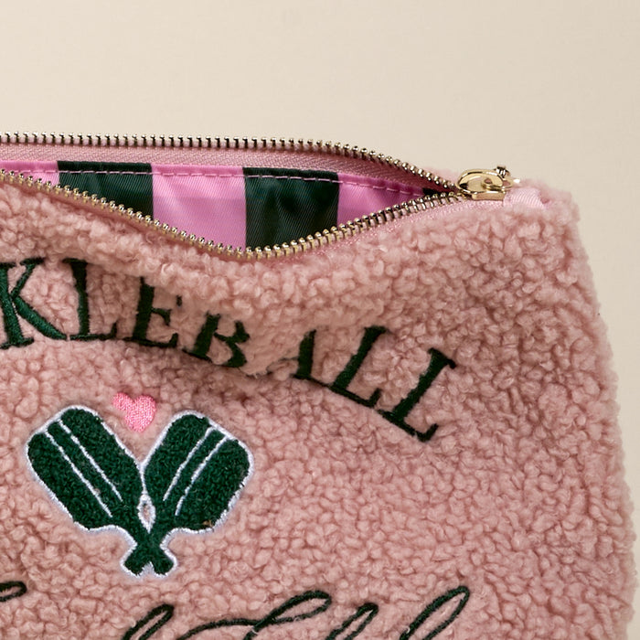 A close-up of The Darling Effect Pickleball Social Club Teddy Pouch shows pink sherpa fabric, green embroidered pickleball paddles, a pink heart, and open zipper revealing a pink and green striped interior—perfect for any accessory set.