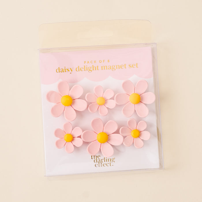 The-darling-effect’s Pink Daisy Delight Magnet Set includes six vibrant pink daisy magnets with yellow centers in clear packaging—perfect for adding charm and securing your notes or photos.