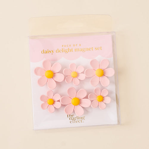 The-darling-effect’s Pink Daisy Delight Magnet Set includes six vibrant pink daisy magnets with yellow centers in clear packaging—perfect for adding charm and securing your notes or photos.