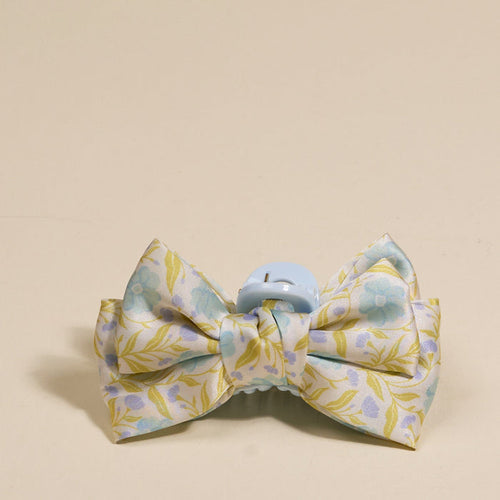 The Darling Effect's Poppin' Petals Aqua Mini Satin Bow Claw Clip features a pastel floral satin bow in light blue, yellow, and green on a light blue clip, displayed against a beige background—a charming hair accessory.