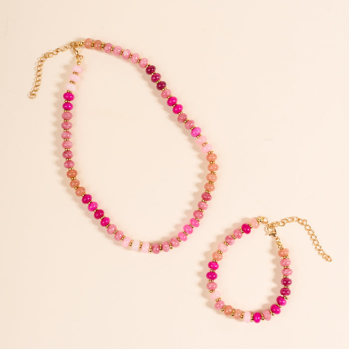 The Darling Effect's Pretty Pinks Stone Candy Necklace set includes a beaded necklace and bracelet with gold clasps and extender chains, featuring round pink and gold beads displayed layered on a light beige background.