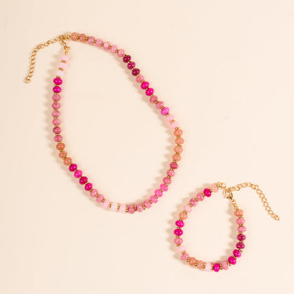The Darling Effect's Pretty Pinks Stone Candy Necklace set includes a beaded necklace and bracelet with gold clasps and extender chains, featuring round pink and gold beads displayed layered on a light beige background.