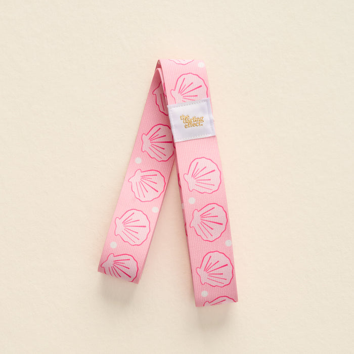 The-darling-effect Put Towel Band-Seashells Pink Stay features a pink no-slip band with white seashells and pink dots, plus a white label. Perfect for keeping your towel secure on your beach chair.
