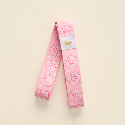 The-darling-effect Put Towel Band-Seashells Pink Stay features a pink no-slip band with white seashells and pink dots, plus a white label. Perfect for keeping your towel secure on your beach chair.
