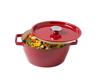 Red enameled cast iron Dutch oven with a lid filled with vegetables on a white background