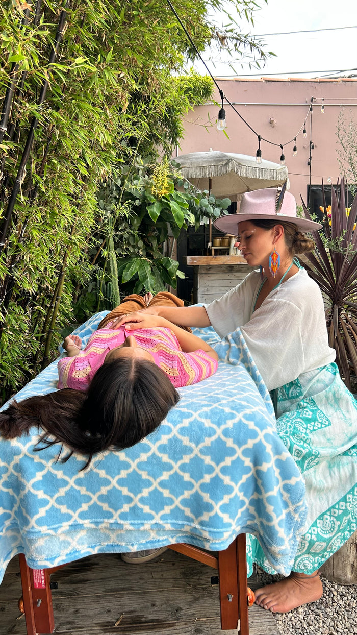 Woman receiving a massage outdoors on a wooden table with a blue and white patterned cover.