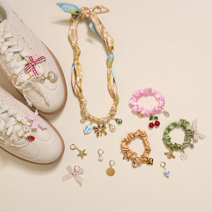 A selection of jewelry and accessories from The Darling Effect, including the Sail Away The Ultimate Charm Pack and a white sneaker with charms and bows, arranged on a light background.