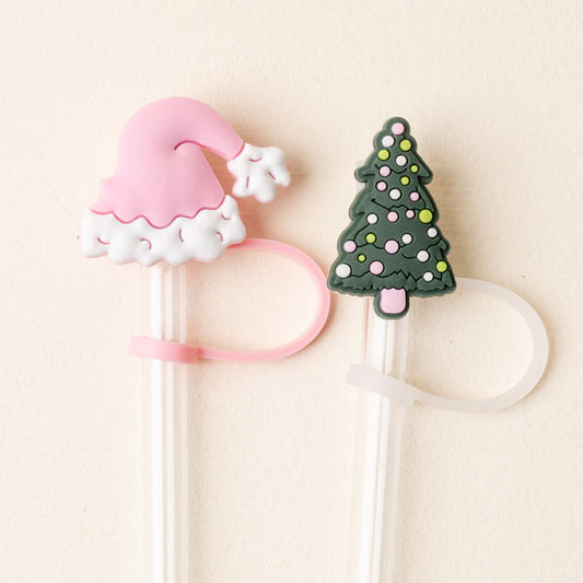 The Darling Effect’s Santa Baby Straw Topper Set includes two white chopsticks with festive silicone toppers—a pink Santa hat and a green ornamented Christmas tree—each with attached loops. Perfect holiday accessories for any drink.