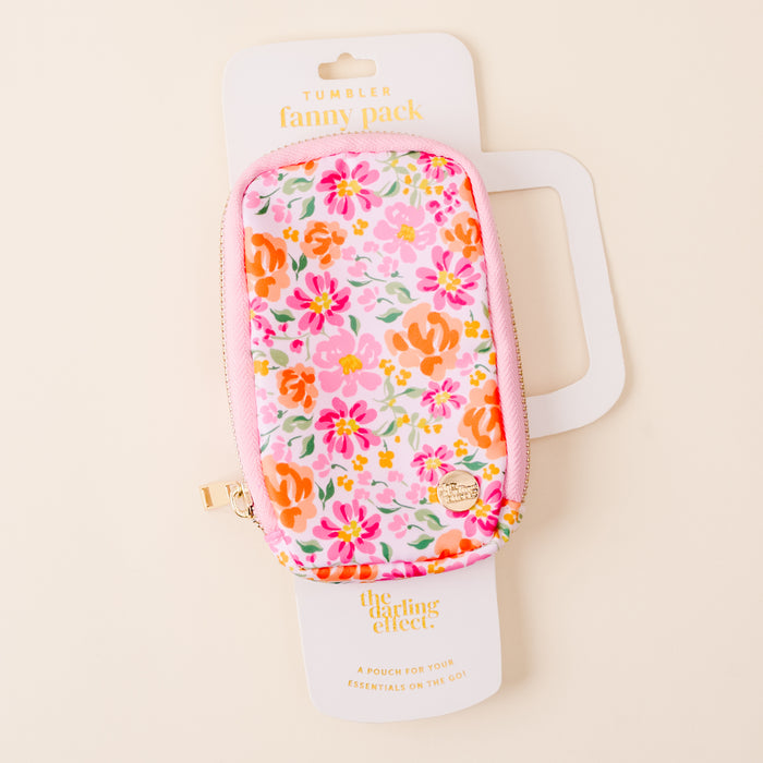 The Secret Garden Pink Tumbler Fanny Pack by the-darling-effect features a colorful floral pattern in pink, orange, and green, is water resistant, and includes a pink zipper with a gold pull. Displayed on white The Darling Effect packaging.
