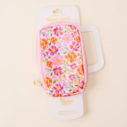 The Secret Garden Pink Tumbler Fanny Pack by the-darling-effect features a colorful floral pattern in pink, orange, and green, is water resistant, and includes a pink zipper with a gold pull. Displayed on white The Darling Effect packaging.