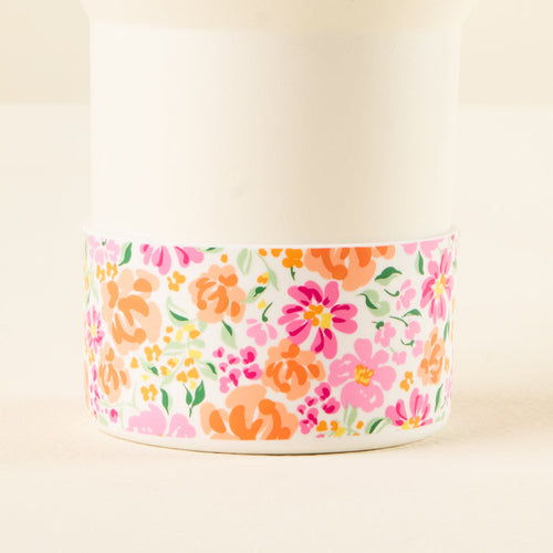 The-darling-effect's Secret Garden Pink Tumbler Silicone Boot features a white cup with a decorative pink, orange, yellow, and green floral band and includes a protective silicone boot to prevent tumbler dents.