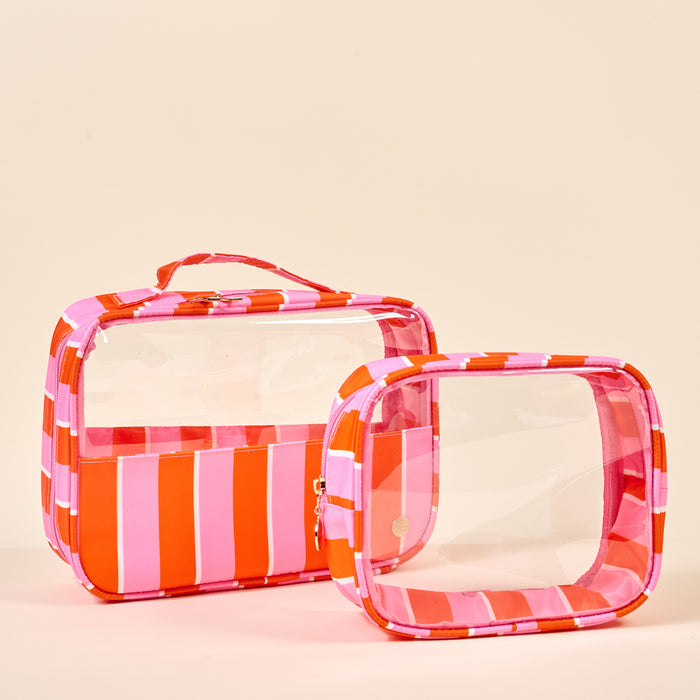 The Darling Effect’s Sicily Stripes Pink Clearly Chic Cosmetic Bag Set includes two clear bags—one large and one small—with pink, red, and white stripes. The larger bag has a striped border and a carrying handle for easy travel.