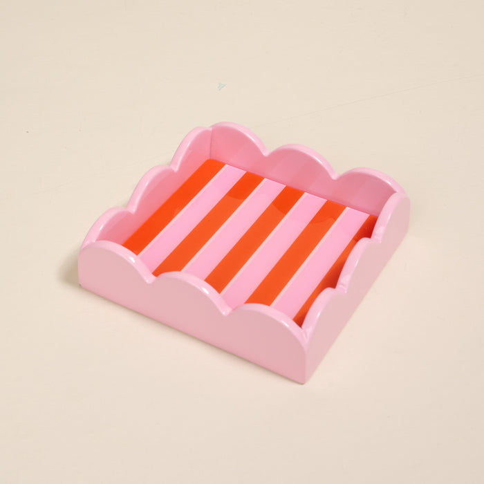 The Darling Effect's Sicily Stripes Pink Scallop Trinket Tray features red and light pink vertical stripes, scalloped edges, and is perfect as a stylish accessory tray on a light beige surface.