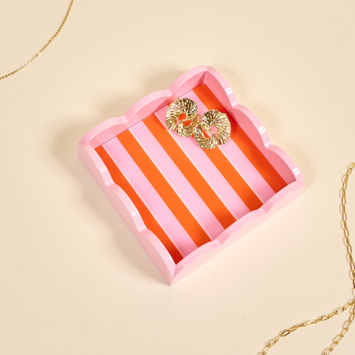The Darling Effect's Sicily Stripes Pink Scallop Trinket Tray, featuring orange and pink stripes, neatly holds ornate gold earrings with a gold chain draped on both sides—making it a chic jewelry organizer.