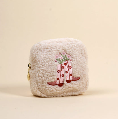 The-darling-effect’s Square Cowgirl Boots Teddy Pouch is a cream-colored sherpa pouch featuring an embroidered design of pink cowboy boots with flowers.