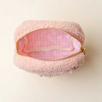 The Darling Effect’s Square Pearl Blush Teddy Pouch is a small, pink sherpa pouch with a gold zipper, pink and white gingham lining, and a mesh pocket inside. Shown open on a light background.