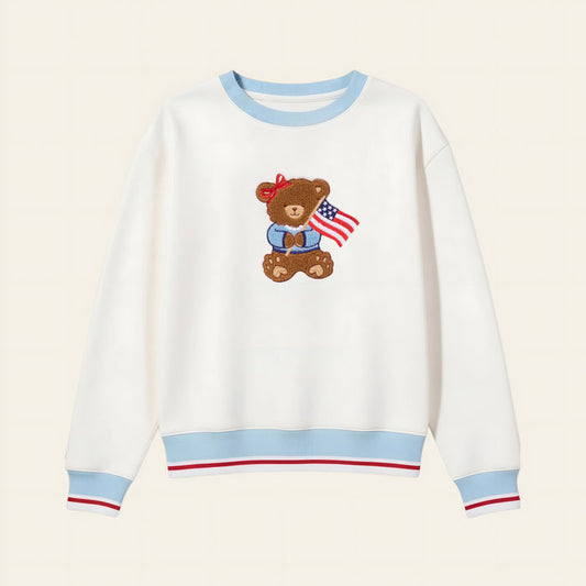 The Darling Effect's Star Spangled Bear Signature Crew features blue cuffs and collar, red stripe accents, and an embroidered teddy bear with an American flag—crafted from soft fabric for everyday comfort.