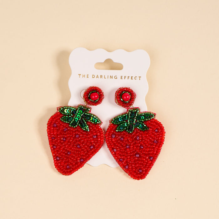 Strawberry Beaded Earrings by The Darling Effect feature green sequin leaves on a pale yellow background—a playful, vibrant addition to your beaded jewelry collection.