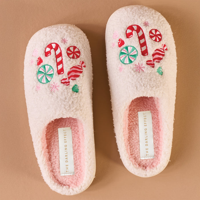 The Darling Effect’s Sugar Rush Fuzzy Slippers are light pink with a plush, fuzzy texture and embroidered candy canes and sweets on top—holiday-ready comfort labeled on the insole.