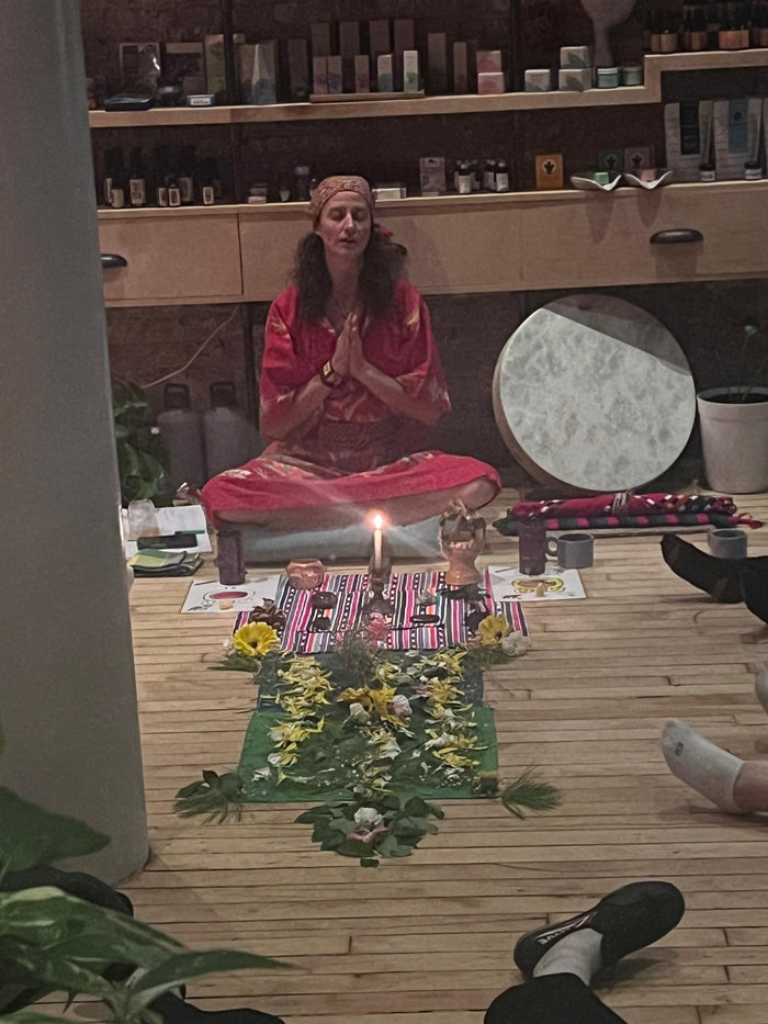 Person in a pink outfit sitting in meditation with candles and flowers on a wooden floor.