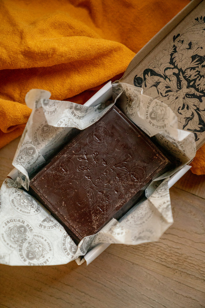 Two chocolate bars in a decorative box on a wooden surface with an orange fabric background.