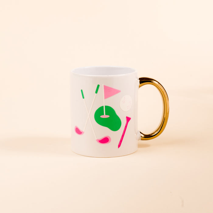 The Golf Edit 11 oz Cozy Cute Ceramic Mug by The Darling Effect showcases pink and green golf-themed art—clubs, flag, tee, and ball—on a pale beige background with a golden handle, perfect for sipping your favorite coffee or tea.