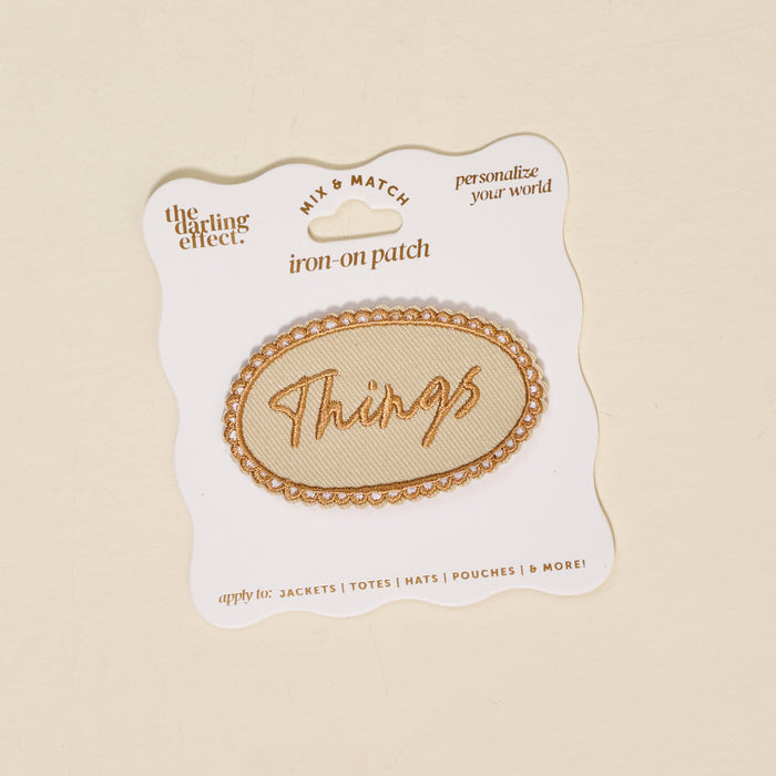 The Darling Effect’s Things Mix & Match Iron-On Patch features an oval shape with gold trim and “Things” in gold script, displayed on a branded card—ideal for adding a stylish, colorful touch to your jackets.