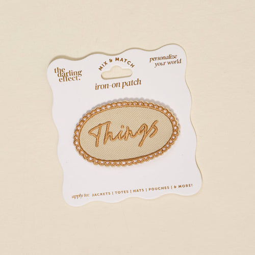 The Darling Effect’s Things Mix & Match Iron-On Patch features an oval shape with gold trim and “Things” in gold script, displayed on a branded card—ideal for adding a stylish, colorful touch to your jackets.