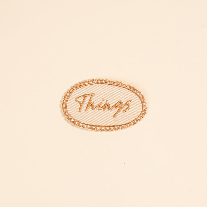The Darling Effect’s Things Mix & Match Iron-On Patch features “Things” in cursive within an oval border on beige—ideal for customizing jackets or adding to your patch collection.