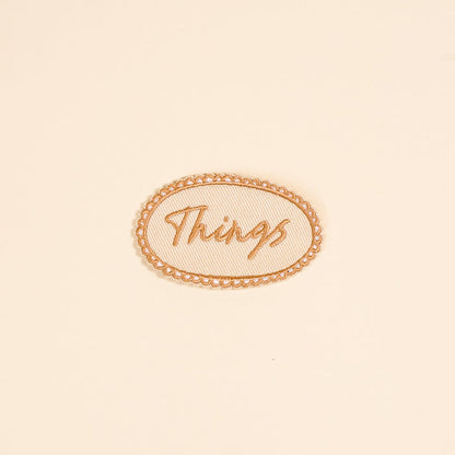 The Darling Effect’s Things Mix & Match Iron-On Patch features “Things” in cursive within an oval border on beige—ideal for customizing jackets or adding to your patch collection.