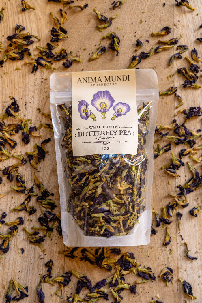 Packaged butterfly pea flowers with Anima Mundi label on a wooden surface with dried flowers.