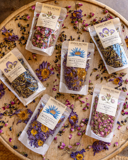 Packaged dried herbs and flowers on a wooden surface with 'Anima Mundi' branding.