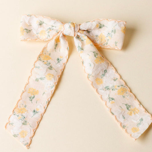 The-darling-effect's Yellow Floral Flair Hair Bow features white and yellow florals, a scalloped peach edge, embellished accents, and a secure gold barrette clip.