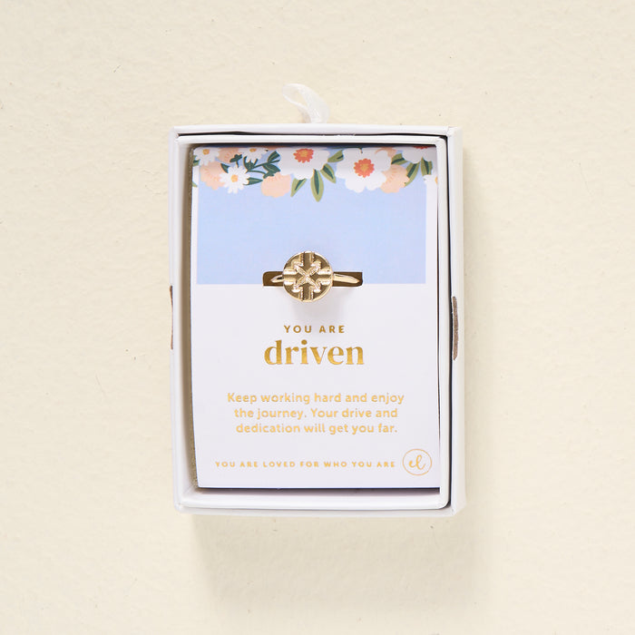 The Darling Effect's You Are Driven Adjustable Ring features a geometric 14k gold design, presented in a white box. Behind it, a floral card reads "You are driven" and shares an inspiring message about hard work and dedication.